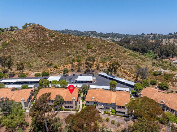 Arial view of residential buildings with orange roofs, surrounded by hilly terrain and parking shades in the background.