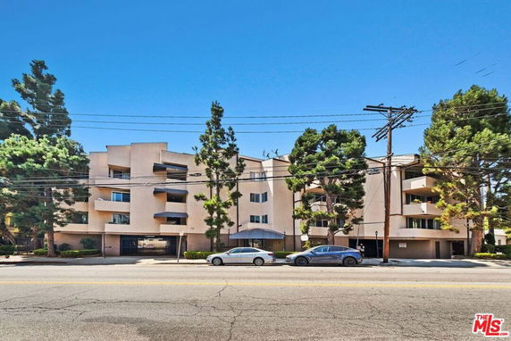 Front view of a multi-story apartment building with balconies and trees around the front.