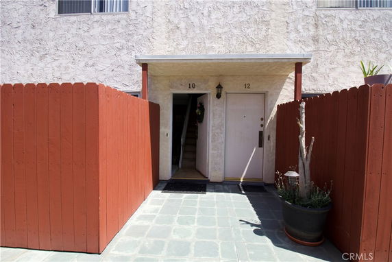 Front view of a building entrance with two doors numbered 10 and 12, surrounded by a wooden fence and tiled walkway.