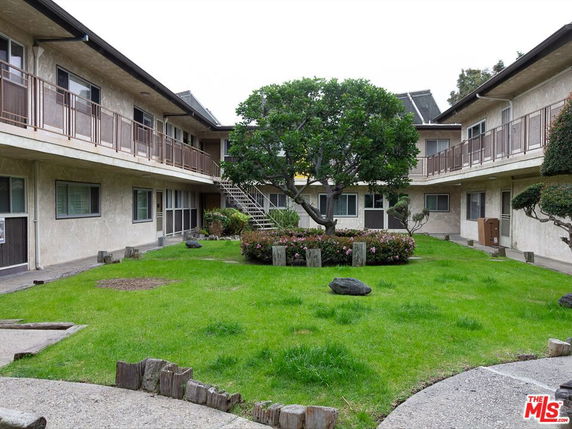 View of a two-story building with an open courtyard featuring grass and trees.