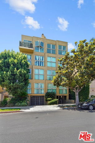 Front view of a multi-story apartment building with large windows and a balcony.