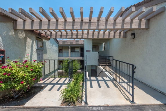 Front view of a residential building entrance with a pergola and railing.
