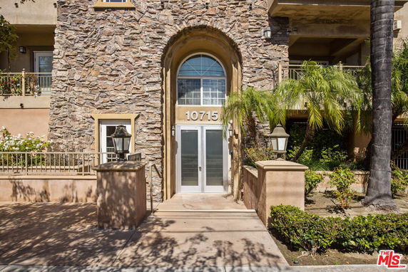 Front view of a stone facade building entrance with a glass door and plants.