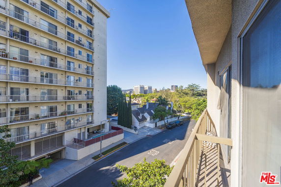 View from a balcony overlooking a street and adjacent high-rise building.