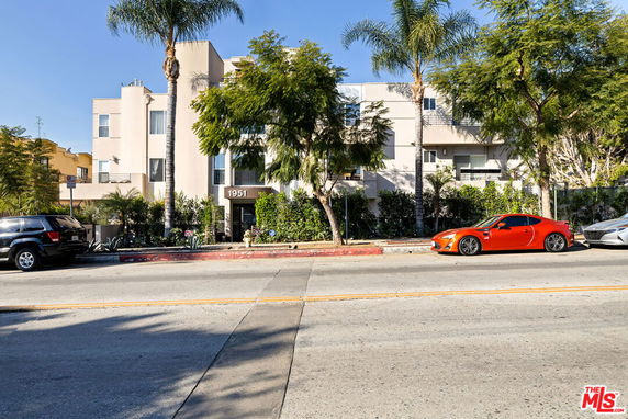 Front view of a multi-story residential building with trees and parked cars.