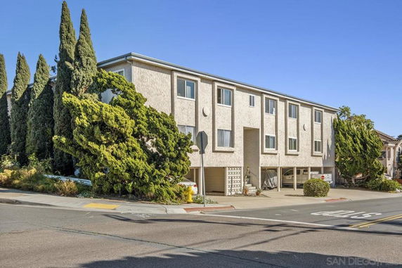 Front view of a multi-story residential building with multiple windows and a partial covered parking area.