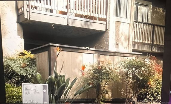 Front view of a building with balconies and plants in the foreground.