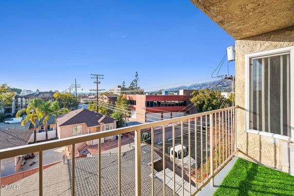 View from a balcony overlooking buildings and a street in an urban area.