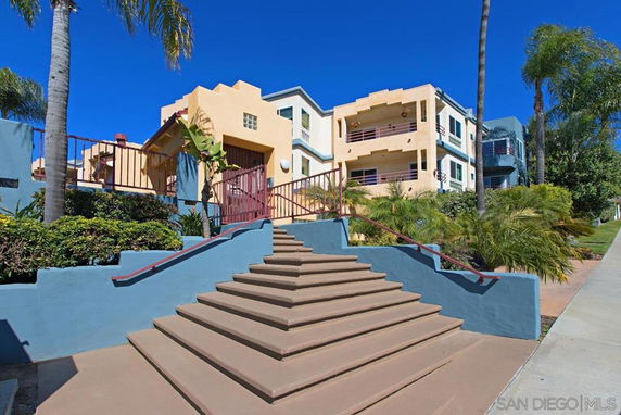 Front view of a multi-story building with balconies and stairway entrance.