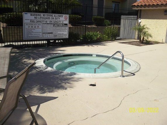 Outdoor view of a small circular swimming pool with a surrounding fence and warning signs.