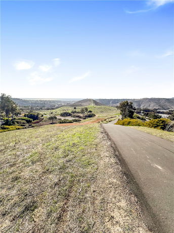 Wide-angle view of a hilly landscape with a road leading through grassy and tree-covered areas.
