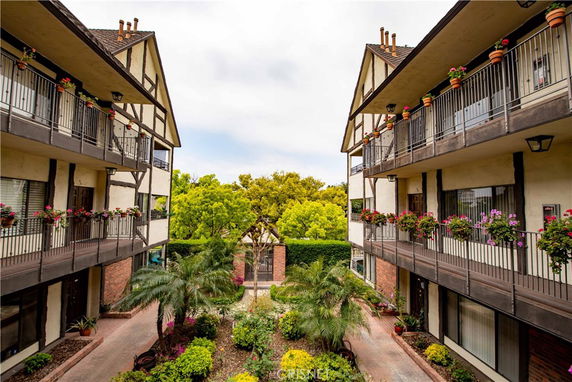 View between two three-story buildings with balconies and flowers, looking out to trees.