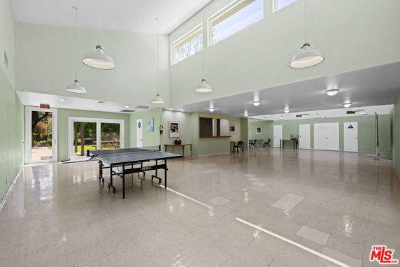 Spacious indoor area with a ping pong table and high ceiling, surrounded by large windows and doors.