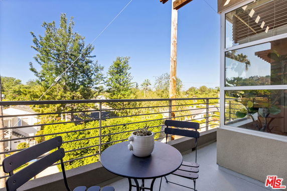 Balcony view with outdoor table and chairs overlooking trees and neighborhood.