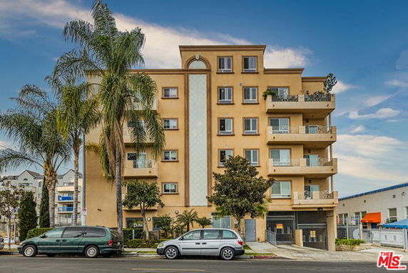 Front view of a multi-story apartment building with balconies and palm trees in front.