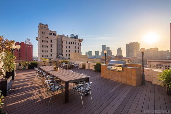 Rooftop area with dining table, chairs, and a grill, overlooking a cityscape.