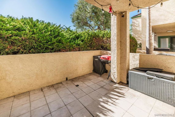 Outdoor patio area with tiled flooring, surrounded by beige stucco walls, and greenery in the background.
