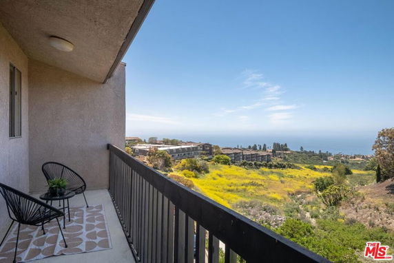 Balcony with chairs overlooking a scenic view of the sea and surrounding landscape.