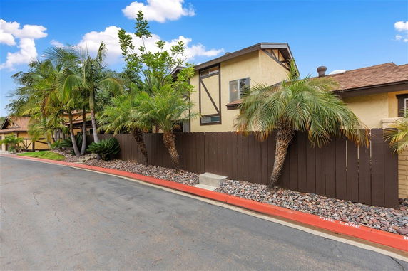 Front view of a two-story house with a brown fence and palm trees.