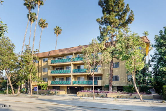Front view of a multi-story apartment building with balconies and a tiled roof.