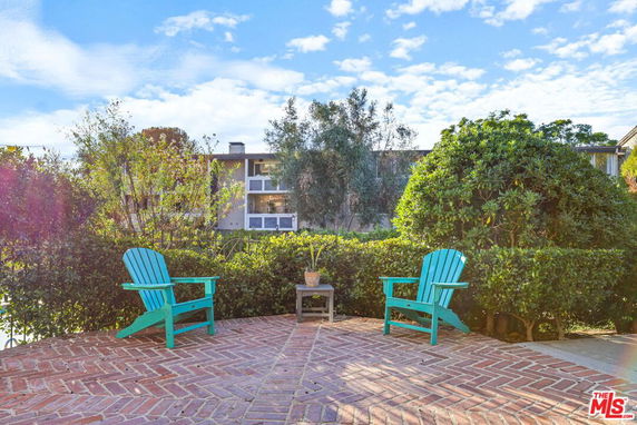 View of a building seen from a patio area with two turquoise chairs and greenery.