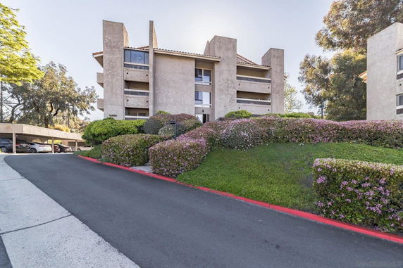 Front view of a multi-story building with balconies and a sloped driveway.