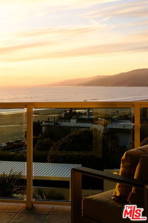 View from a balcony with ocean and mountainous landscape in the background at sunset.