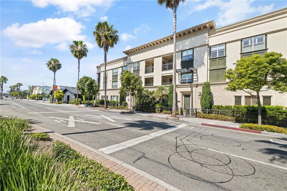 Front view of a multi-story building with balconies and palm trees lining the sidewalk.