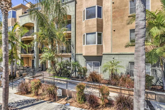 Front view of a multi-story residential building with balconies and prominent landscaping.