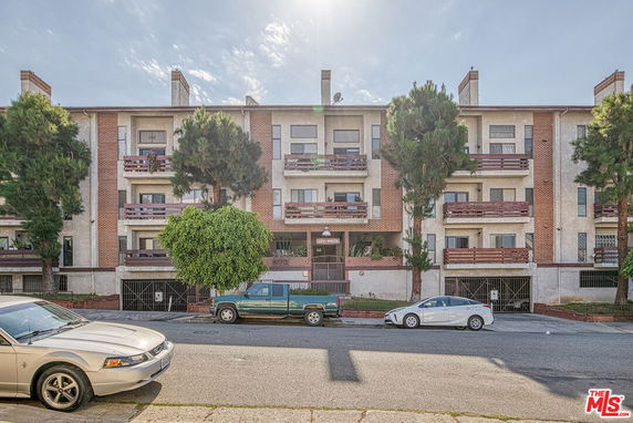 Front view of a multi-story apartment building with balconies and trees in front.