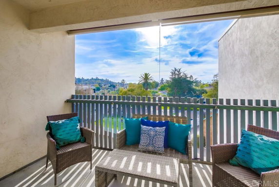 Balcony with outdoor seating and view of distant trees and sky.