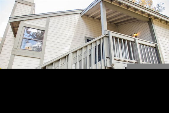 View of a house exterior with a sloped roof and wooden railing.