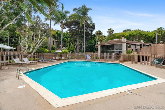 Outdoor swimming pool with surrounding fence and poolside chairs.
