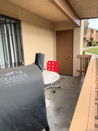 View of an outdoor balcony area with a grill and a small table with a red chair.