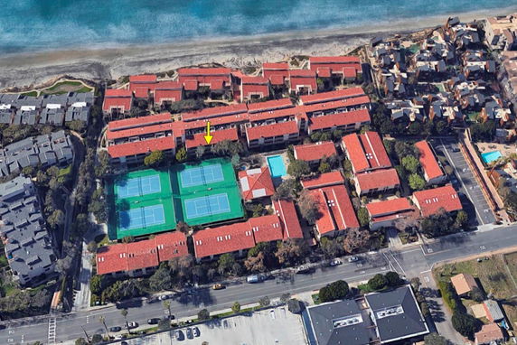 Aerial view of a complex with multiple tennis courts and residential buildings near a beach.