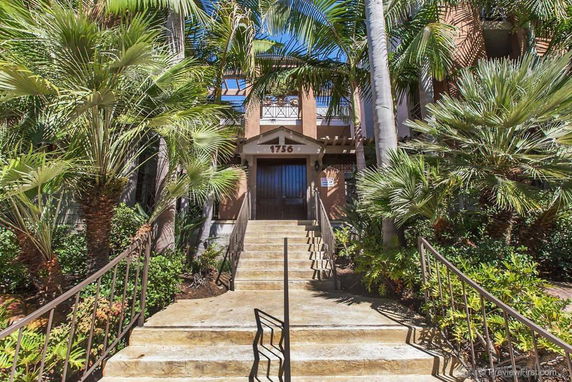 Front view of a residential building with stairs and palm trees.