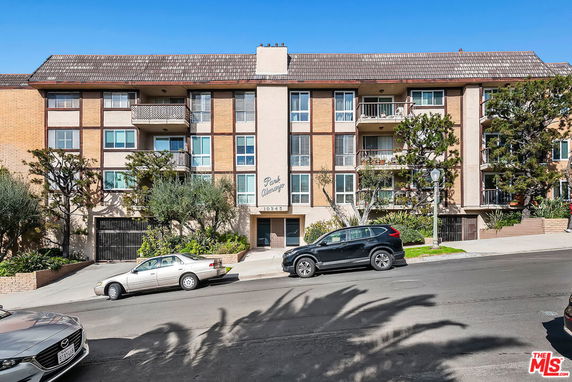 Front view of a multi-story apartment building with balconies and a pitched roof.