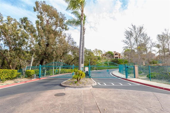 Gated entrance with road leading up to a house in a wooded area.