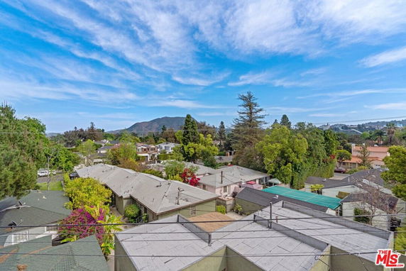 Panoramic view overlooking residential rooftops with trees and mountains in the background.