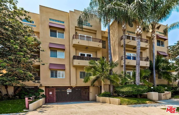 Front view of a multi-story residential building with balconies and palm trees.