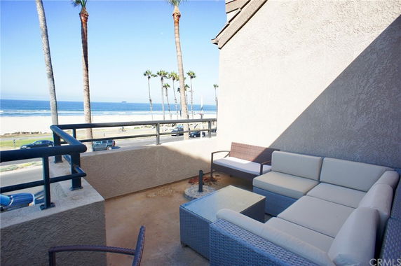 View of a beach with palm trees and ocean from a balcony with outdoor seating.