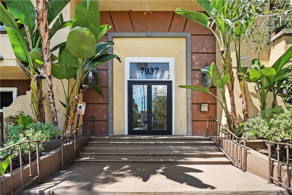 Entrance view of a building with a glass double door and surrounding plants.