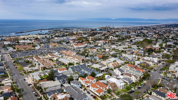 Aerial panoramic view of a coastal town with numerous buildings, streets, and the ocean in the background.