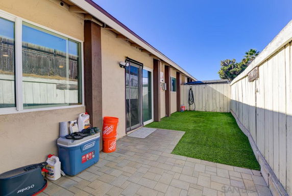 Backyard area with artificial grass and pavers, alongside a house with sliding glass doors.