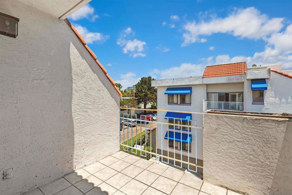 View from a balcony showing neighboring buildings with orange-tiled roofs and blue awnings.