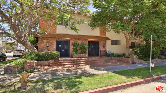 Front view of a two-story house with brick and stucco exterior and large trees in front.