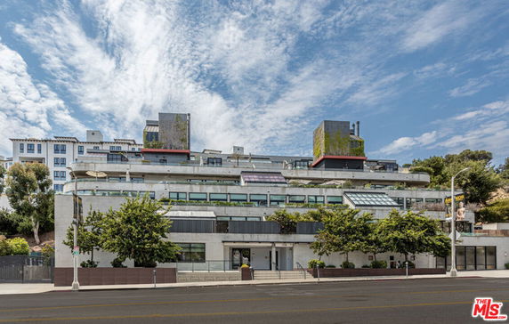 Front view of a multi-story building with a modern design and greenery on the upper levels.