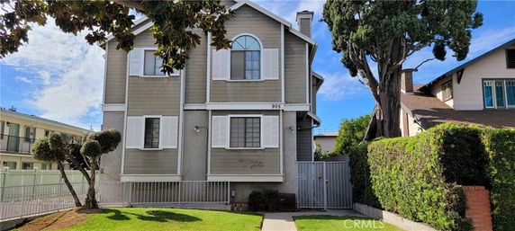Front view of a two-story house with a gray facade, white window shutters, and a gated entrance.