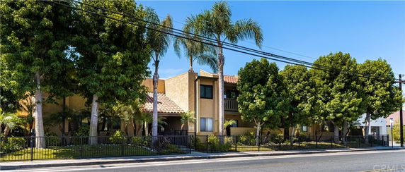 Front view of a multi-story residential building with a tiled roof and balcony, surrounded by trees.