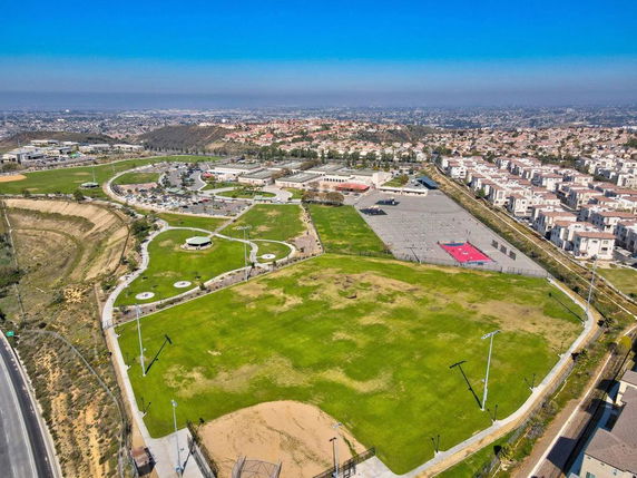 Wide angle view of landscape with residential area, open green spaces, and distant cityscape.